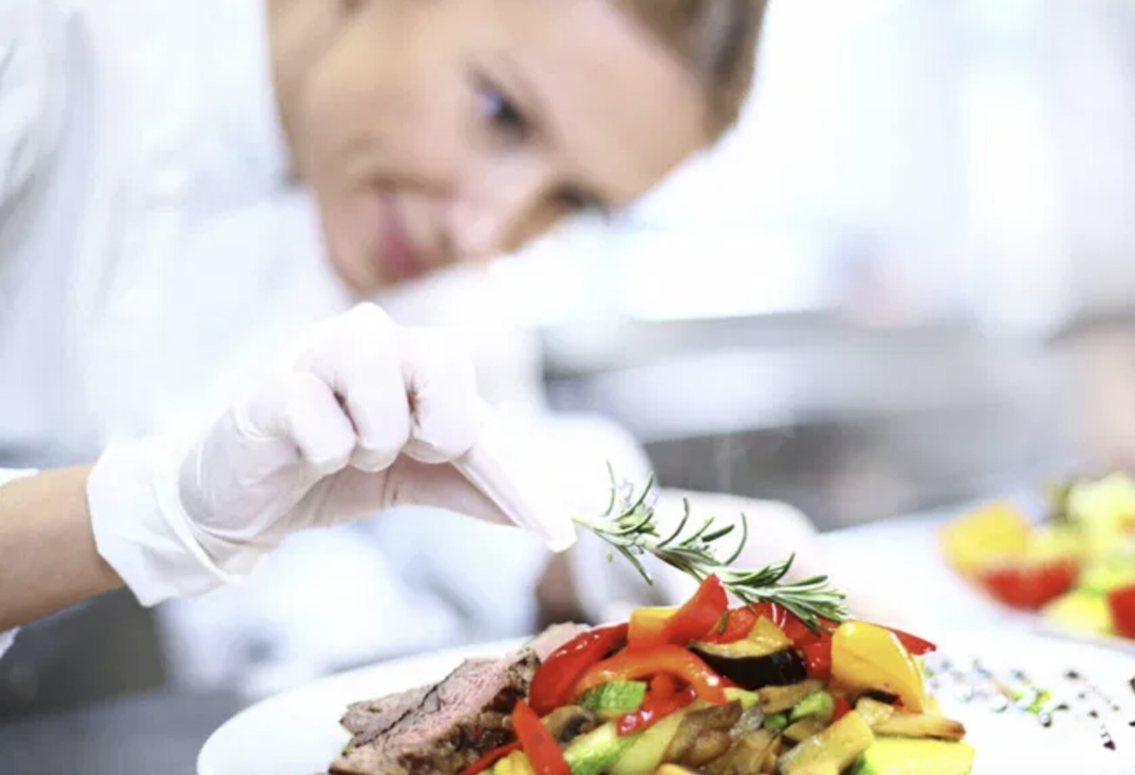 A professional chef focused on garnishing a vibrant vegetable dish with fresh rosemary, creating a visually stunning presentation.